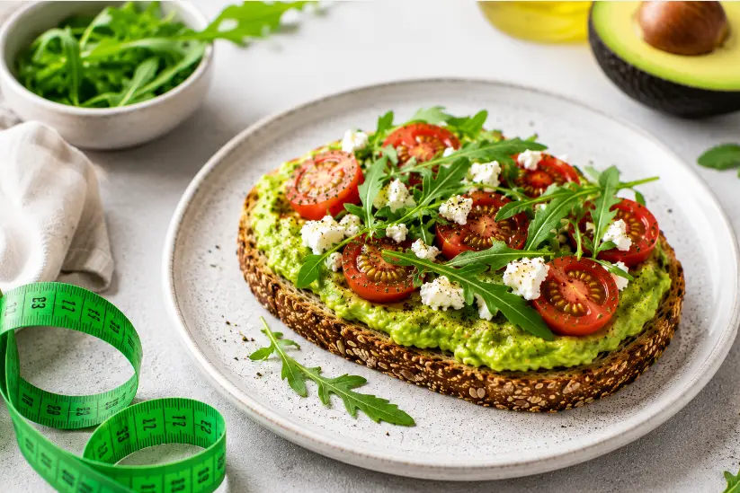 Avocado toast con pane integrale, avocado fresco, pomodorini, formaggio fresco e rucola, fotografato in stile food photography per un articolo su alimentazione equilibrata.